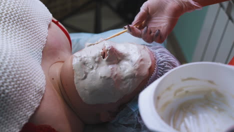 woman applies alginate mask to plus-size girl with spatula