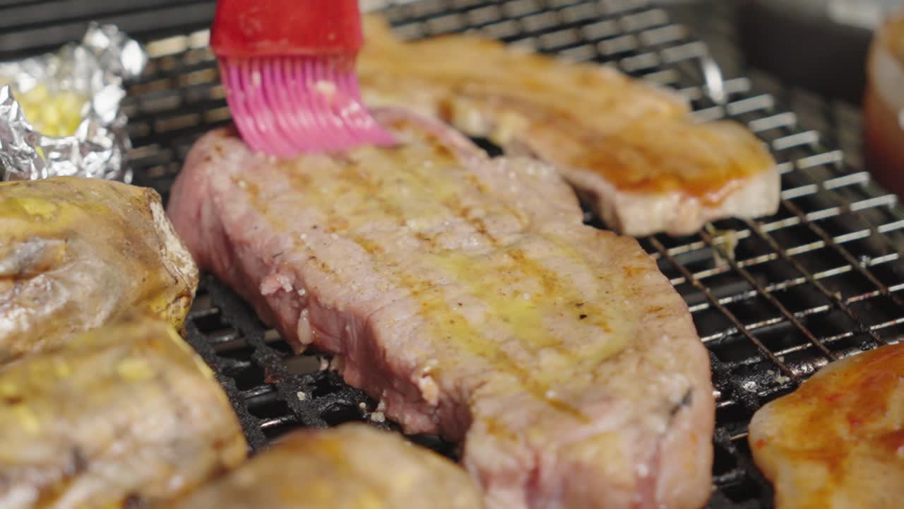 Close up shot of a sirloin steak being buttered with a brush by the chef's hand