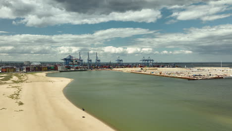 Vista-Aérea-De-Una-Playa-De-Arena-Junto-A-Una-Zona-Portuaria-Industrial-Bajo-Un-Cielo-Nublado---Gdańsk,-Polonia