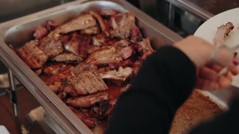 grilled meat cuts in a buffet tray with hand using tongs to serve portion