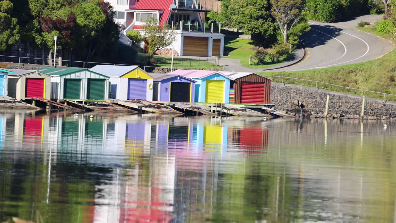 Vibrant sheds reflecting on calm waters in Akaroa