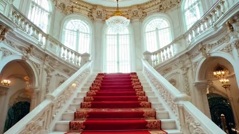 A red carpeted staircase in a large building with a chandelier
