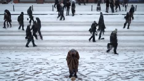 a bustling city street is covered in snow as people hurry by in winter clothing. in the foreground, an individual kneels on the ground, seemingly focused on something.
