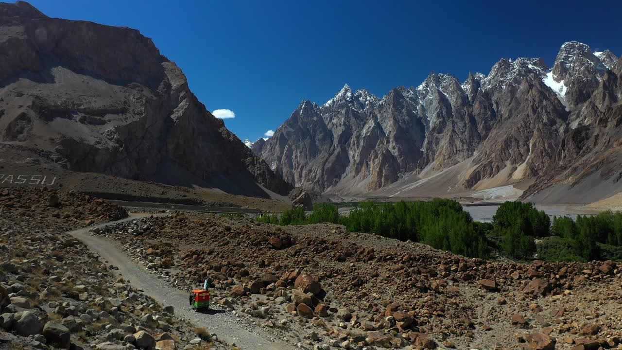 toma cinematográfica de un tuk-tuk en un camino de grava en la autopista karakoram pakistán con los conos passu en la distancia