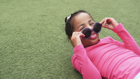 In-a-school-setting,-a-young-African-American-girl-lies-on-the-grass-with-copy-space