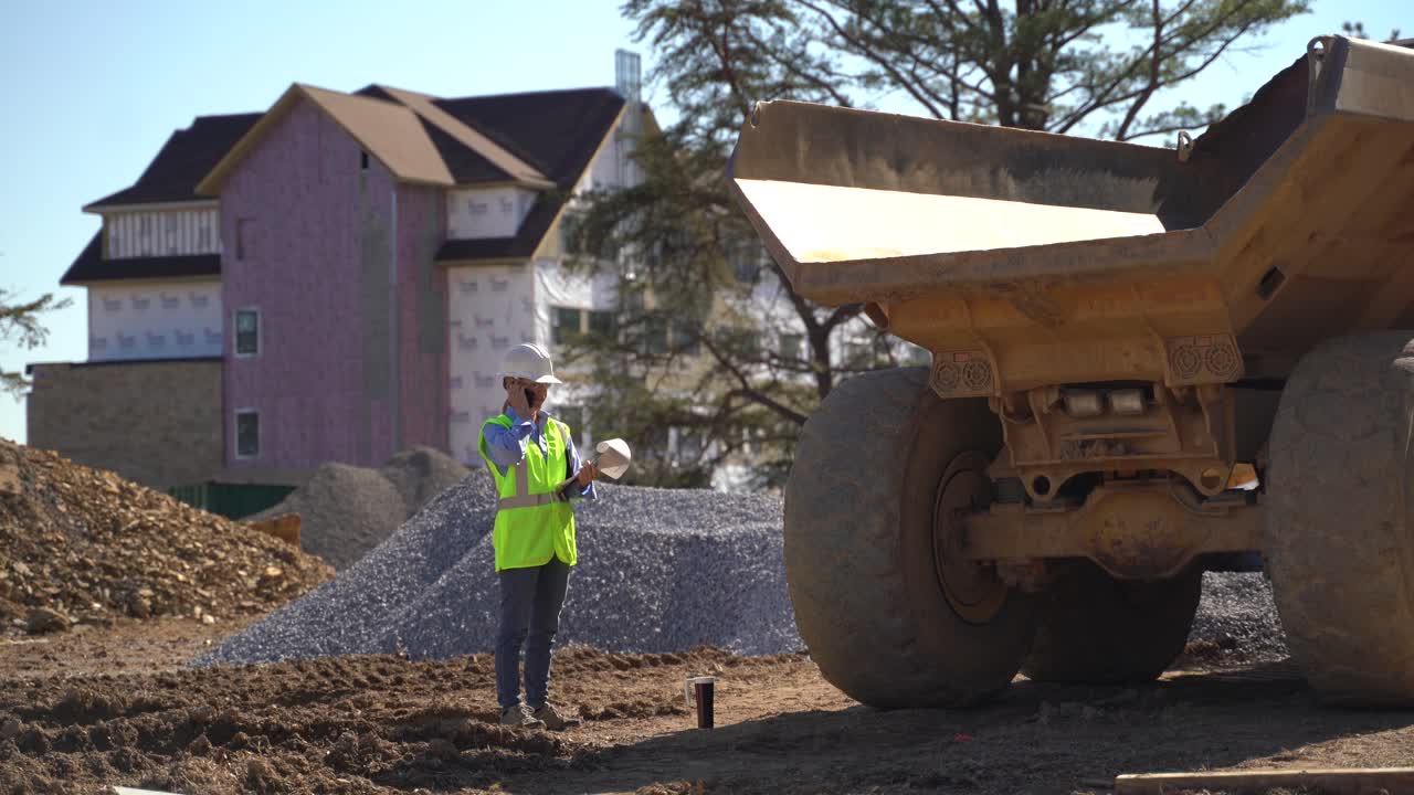 mujer ingeniera gerente de proyecto usando un teléfono inteligente y un portapapeles en un sitio de construcción hablando con colegas y revisando el progreso del trabajo