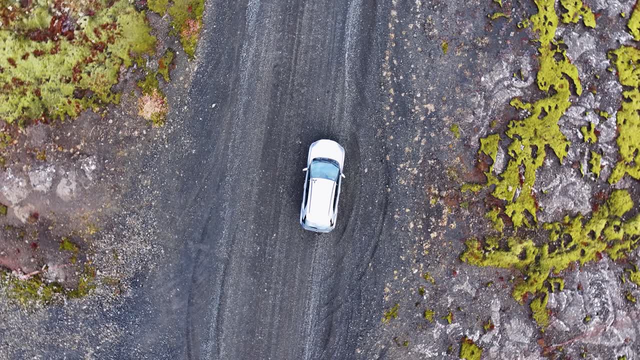 Riprese aeree mostrano un'auto bianca parcheggiata in un terreno desolato da una prospettiva a spirale di un drone.