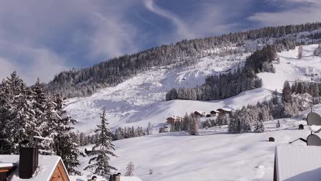 sapins et toits de maisons enneigées au premier plan et pistes de ski et remontées mécaniques dans les alpes italiennes montagnes pleines de neige après une forte chute de neige