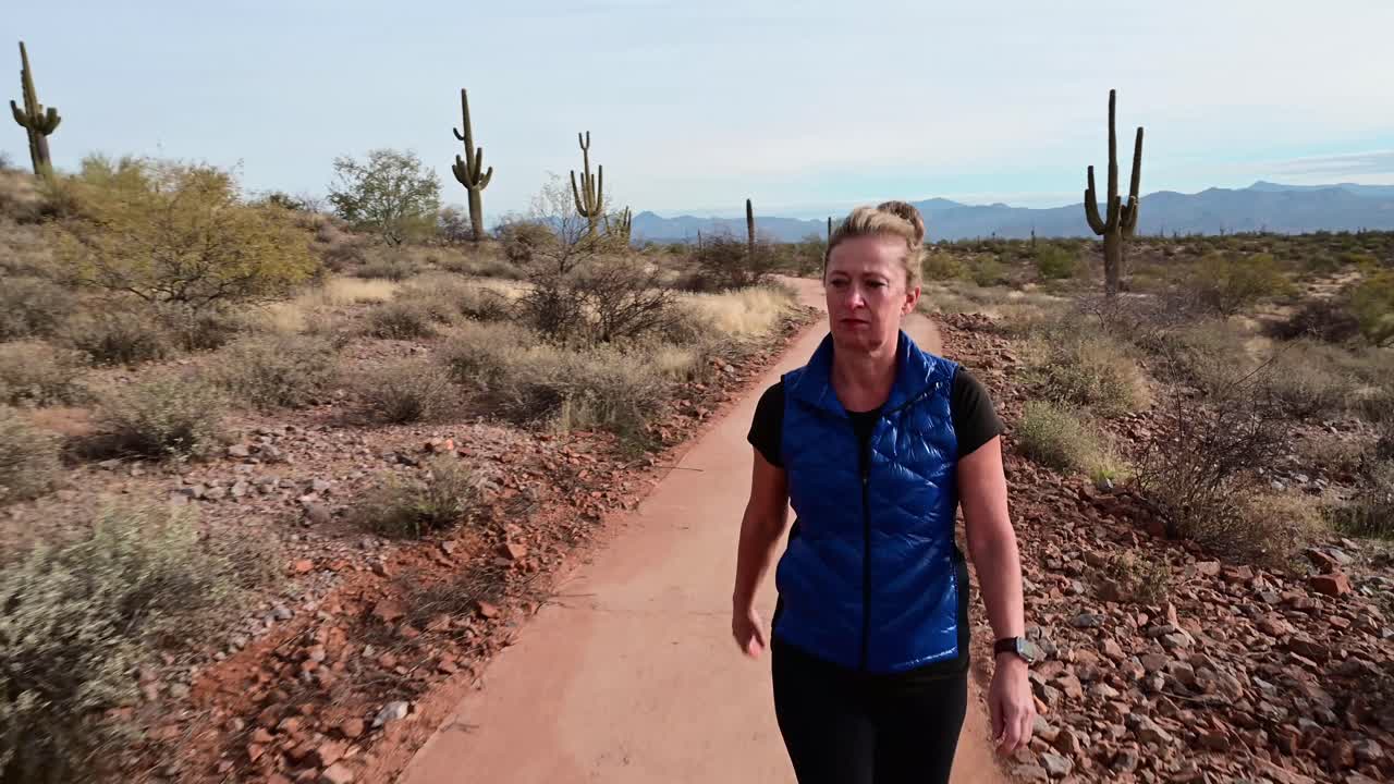 mujer caminando por un sendero pavimentado en un paisaje desértico