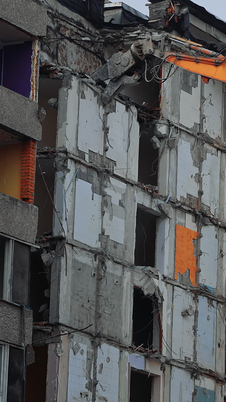 Top floors destruction by the hydraulic claw of excavator. Demolition of old house building for new construction by excavator bucket. View from the below. Vertical video