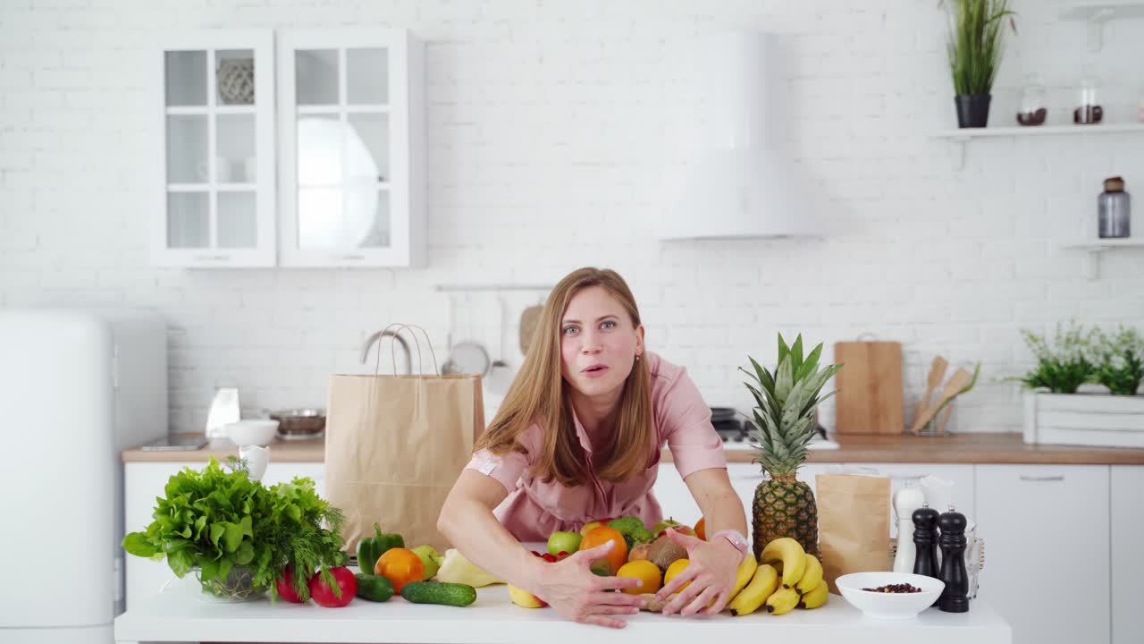 Happy woman unpacking healthy vitamins. Young female in the kitchen at home. Smiling housewife near the table with a lot of fresh fruit and vegetables. Diet lifestyle.