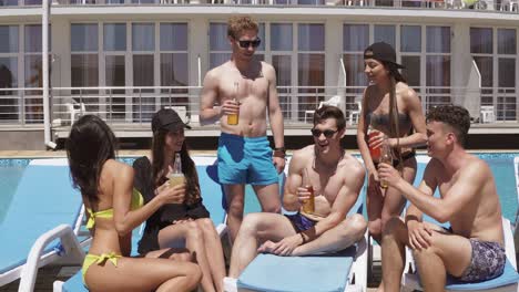 group of beautiful young friends in swimsuits drinking cocktails with cheers and having fun sitting by the swimming pool. shot in 4k