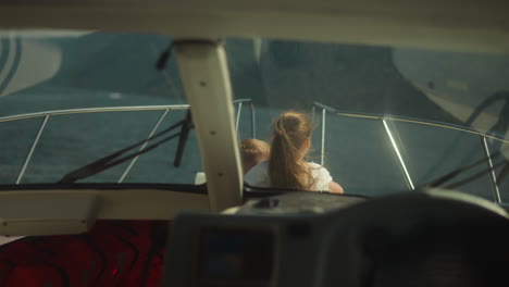 girl points forward riding motorboat with junior brother view from cockpit. happy children enjoy exotic landscape sailing modern yacht on holiday