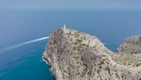 Aerial---boat-in-turquoise-water-bay-near-cliff-with-lighthouse,-Mallorca