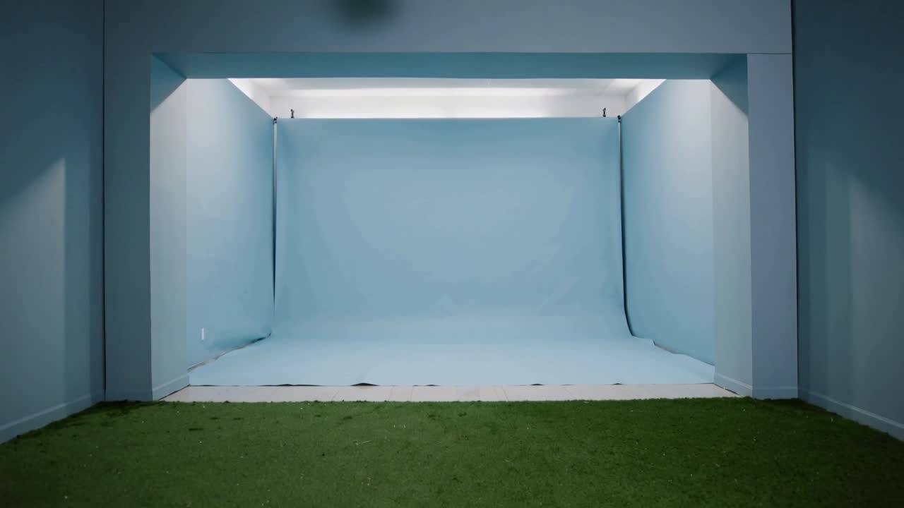 Brightening lights revealing light-blue curved cyclorama backdrop in studio bay, with green turf