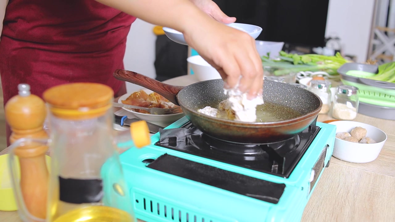 Koki Menempatkan Potongan Tuna Berbalut Adonan ke Wajan Panas Berisi Minyak di Atas Kompor Portabel