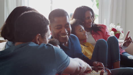 Three-generation-African-American-family-sitting-on-sofa-watching-TV-and-eating-popcorn-together,-close-up