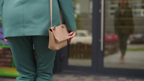 Elegant-woman-in-green-jacket-walks-towards-big-glass-door