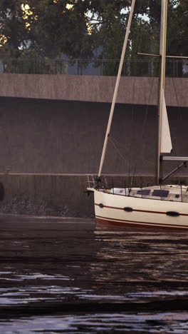 sailboat docked in quiet waters near urban shoreline at dusk