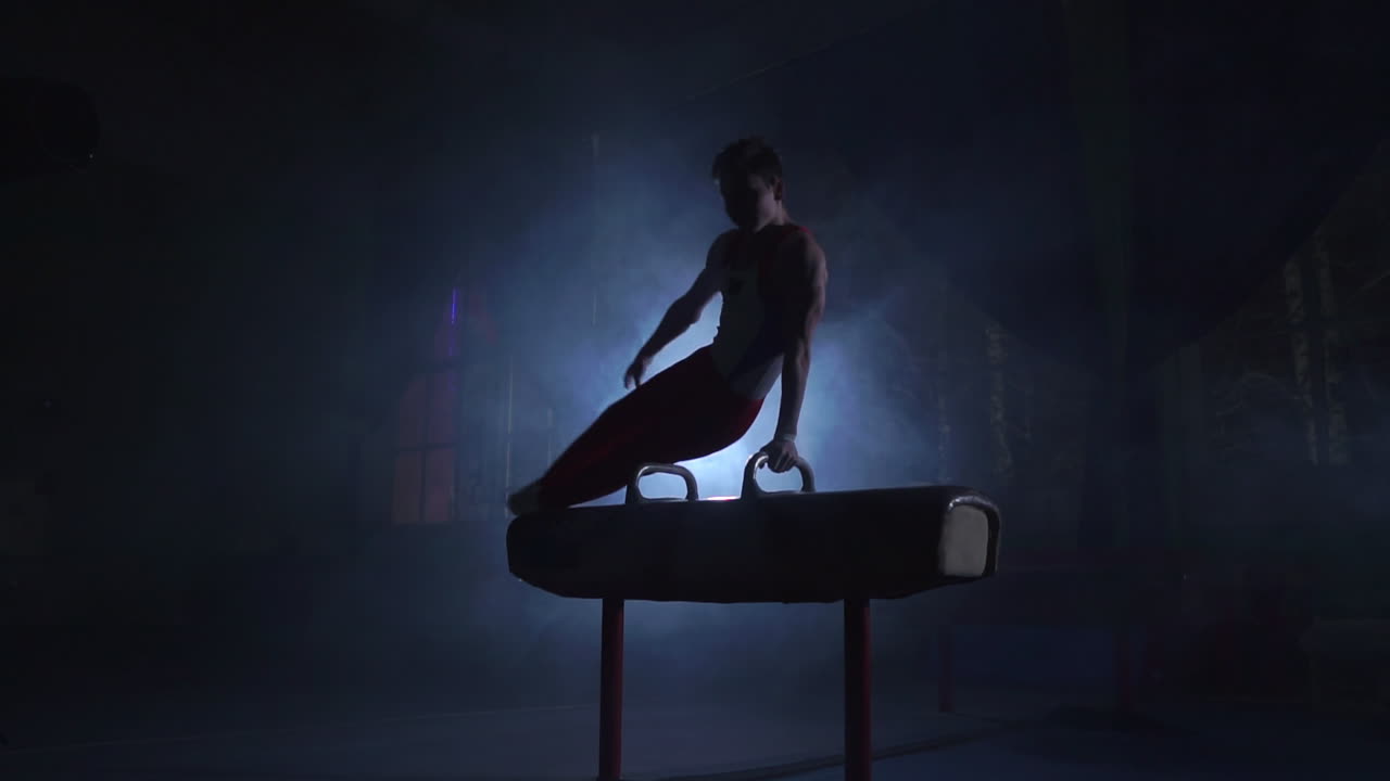 male gymnast athlete performs handstand and spin on Pommel horse on a dark background and smoke in slow motion. Olympic programme
