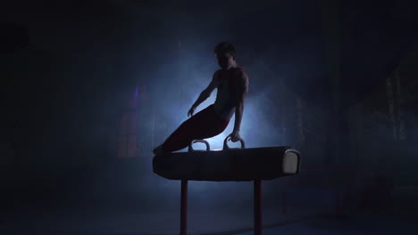 male-gymnast-athlete-performs-handstand-and-spin-on-Pommel-horse-on-a-dark-background-and-smoke-in-slow-motion.-Olympic-programme