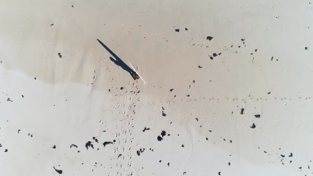 해변에서 서핑보드를 들고 달리는 남자의 최고 전망과 그 옆에 서핑보드를 내려놓는 동안 멈춘다