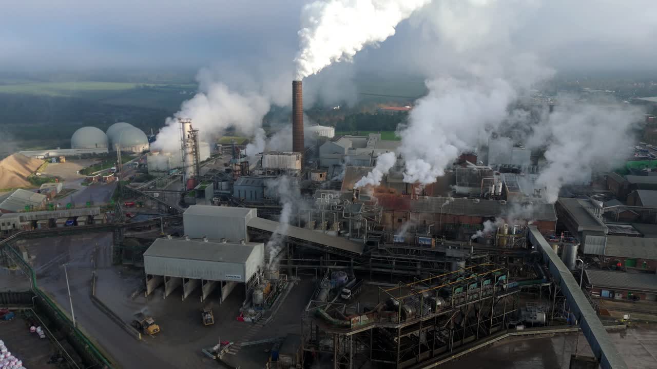 Cinematic drone flight over expansive British Sugar processing plant in Bury St Edmunds featuring industrial silos and white smoke plumes