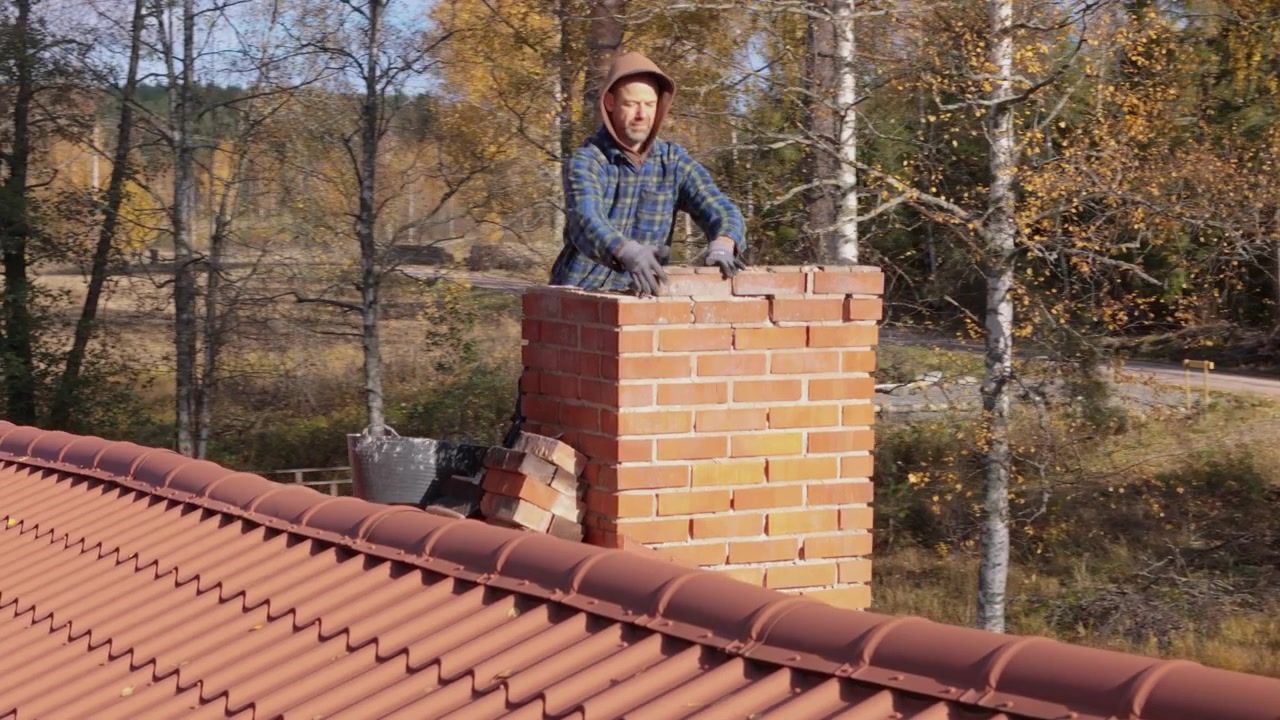 Handyman på hustag, der demonterer en ødelagt murstensskorsten, tæt luftfoto