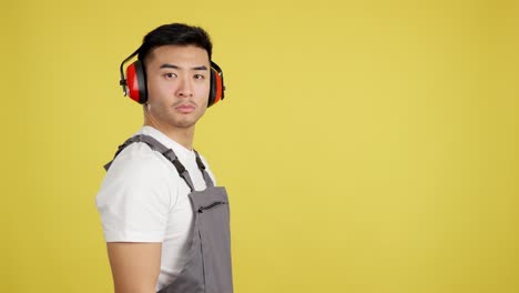 asian man worker in overalls with ear protection on yellow background