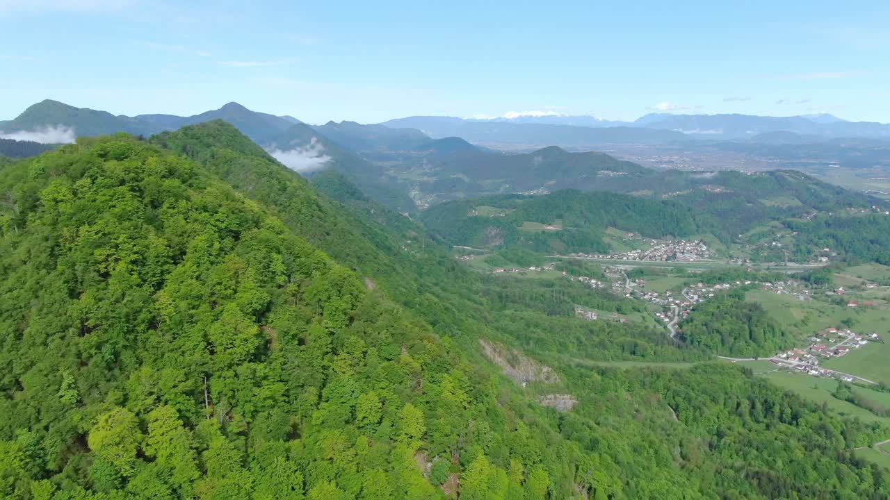 Green lush trees on side of mountain and panoramic view of city and mountain range, Slovenia, aerial