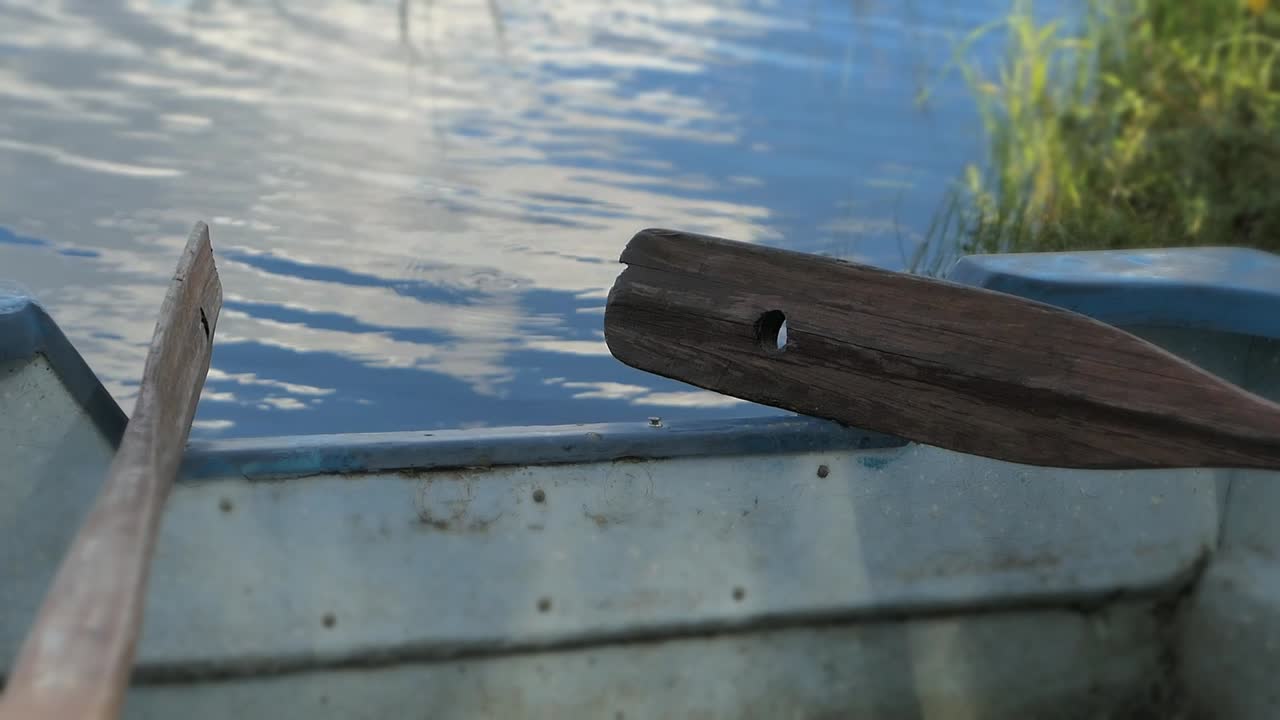 Paddles against boat on shore by calm water, boat by lake oars close up