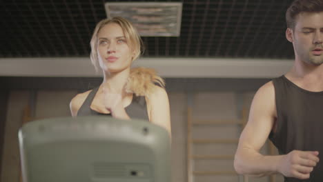 Concentrated-sport-couple-talking-in-gym.-Closeup-couple-running-on-treadmill