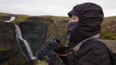 warmly wrapped woman takes a photo with a professional camera at the haifoss waterfall in iceland