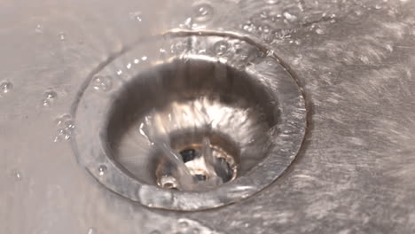 close up slow motion shot of water draining down a stainless steel sink