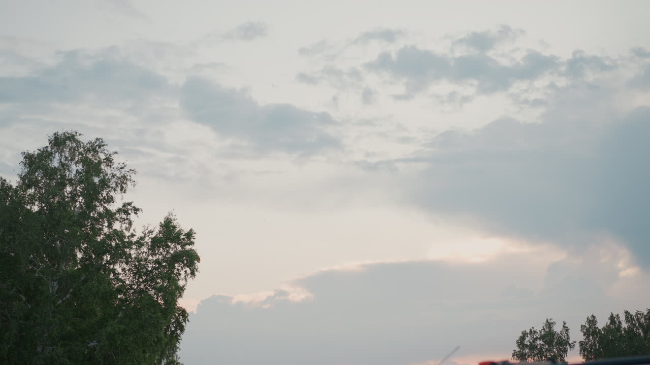 powered paraglider soaring over vast grass field at dusk under moody pastel sky, red canopy lit against fading light, pilot silhouetted below wing, aerial adventure in countryside setting