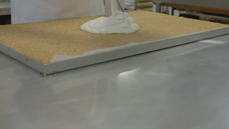 pan up of a worker adding icing mix to a factory size tray of flapjack or granola bar