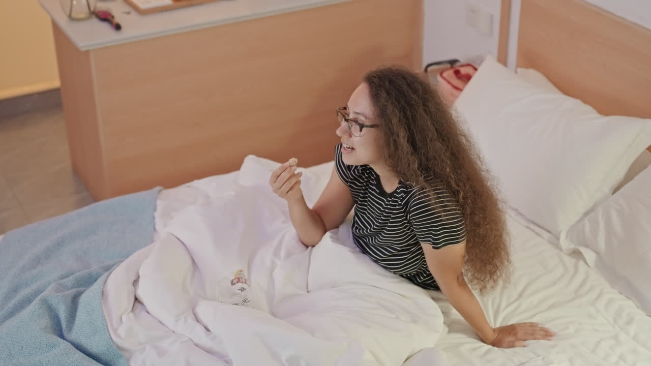Woman enjoying solitude. Woman unwinding alone in hotel room with snacks and light. Individual woman peacefully enjoying late night snack while browsing her phone in cozy hotel surroundings