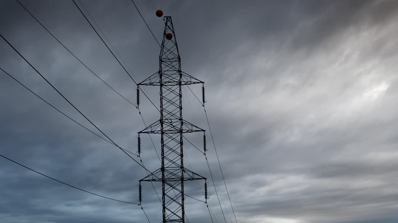 Electrical transmission tower against moving storm clouds time-lapse, electricity pylon and high voltage power lines with dramatic clouds