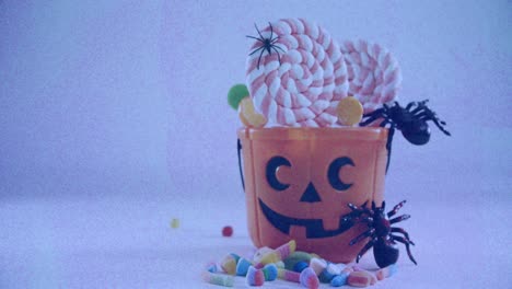 Spiders-and-candies-in-halloween-scary-pumpkin-bucket-against-textured-white-background