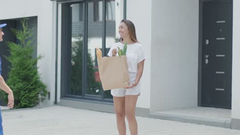 beautiful woman meets a delivery man who gives her a shopping package with food beside her home. food delivery. concept of courier, home delivery, online shopping