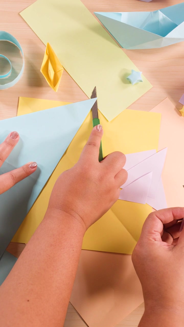 Vista dall'alto di mani che usano le forbici per tagliare carta pastello per vari progetti di artigianato origami