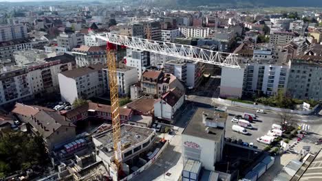 Drone-Shot-of-a-Crane-in-a-Construction-Site-with-a-Cityscape-behind