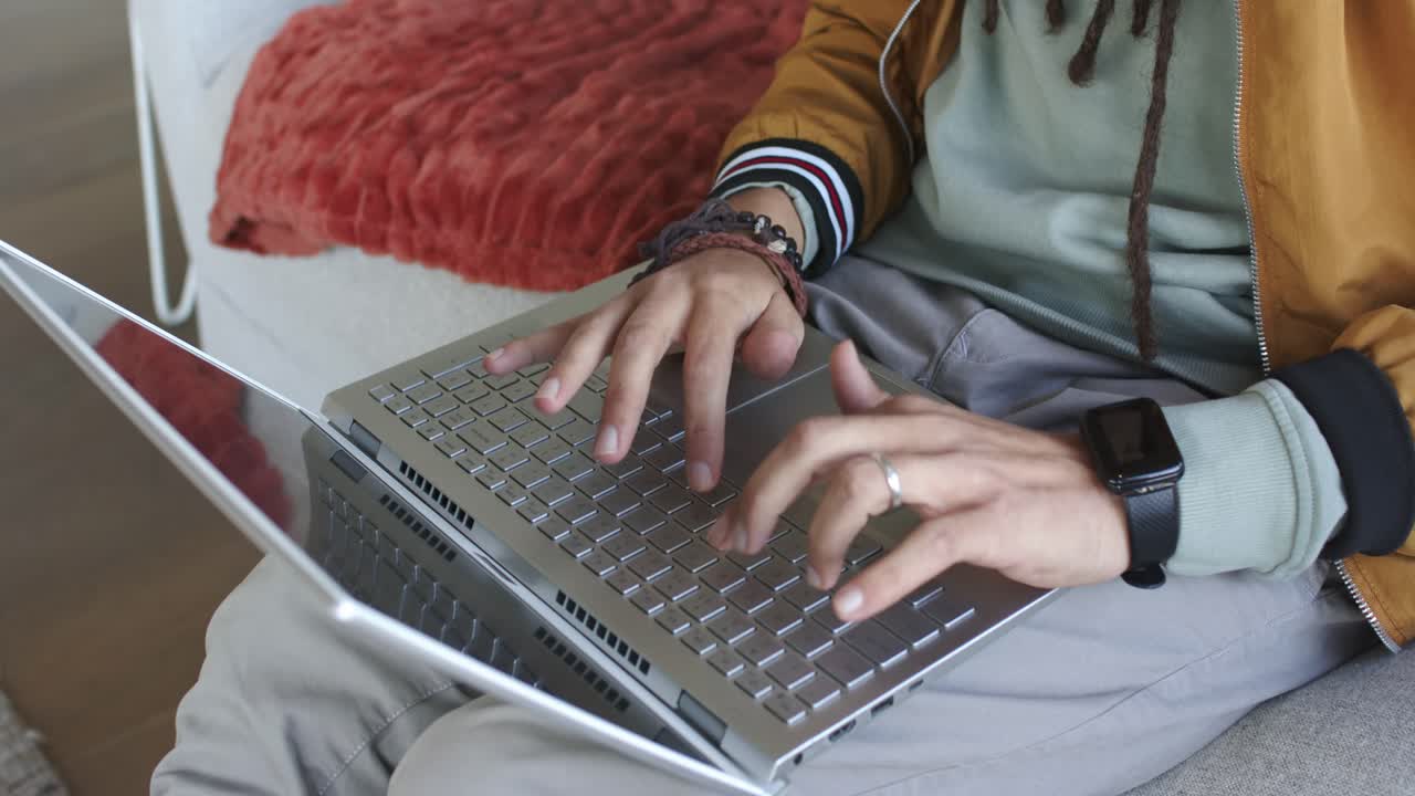 Man is opening silver laptop lid and typing for work on grey sofa near red cushion