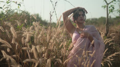 woman in pink dress posing thoughtfully in sunlit field of tall grass, soft focus, natural light