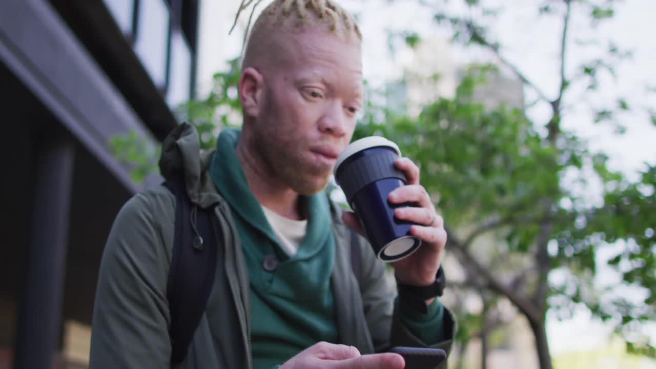 hombre albino afroamericano pensativo con rastas bebiendo café y usando un teléfono inteligente