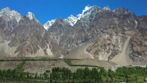 cinematic drone shot of tupopdan peak from the valley, passu cones in hunza pakistan, snow covered mountain peaks with steep cliffs, wide panning aerial shot