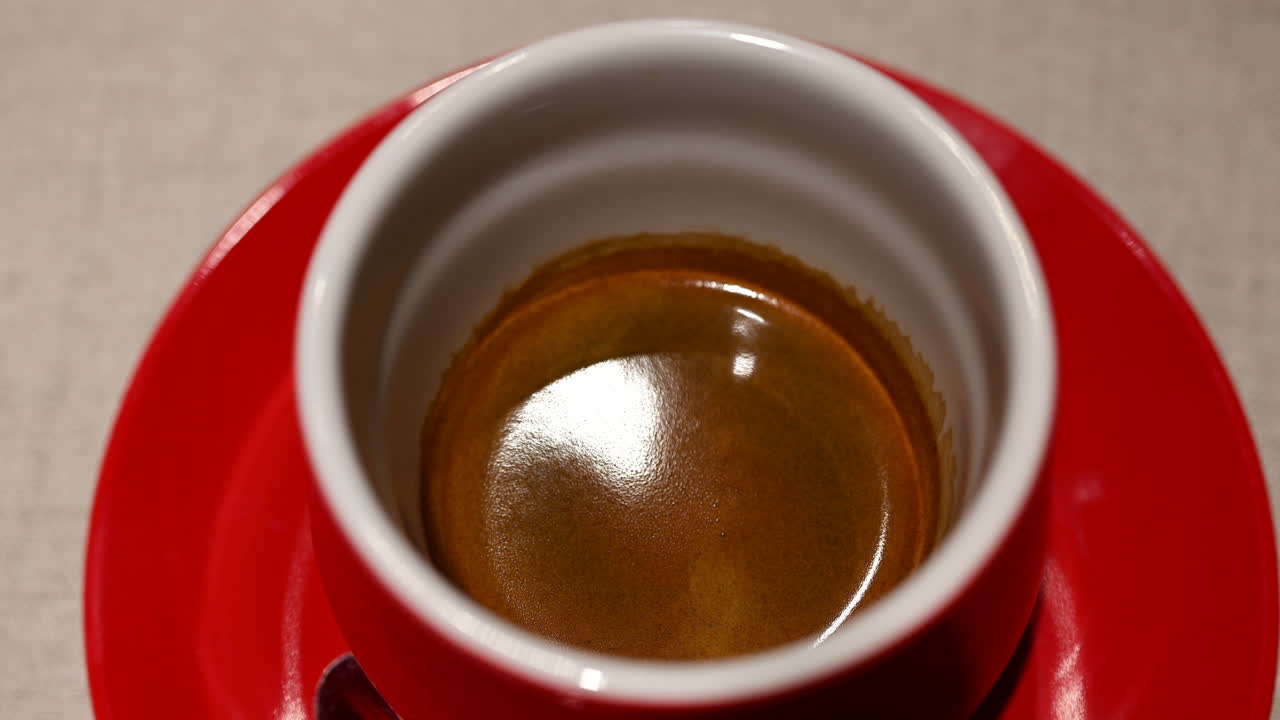 Caffè espresso fresco servito in una tazza di ceramica rossa con crema in superficie, in un ambiente da bar