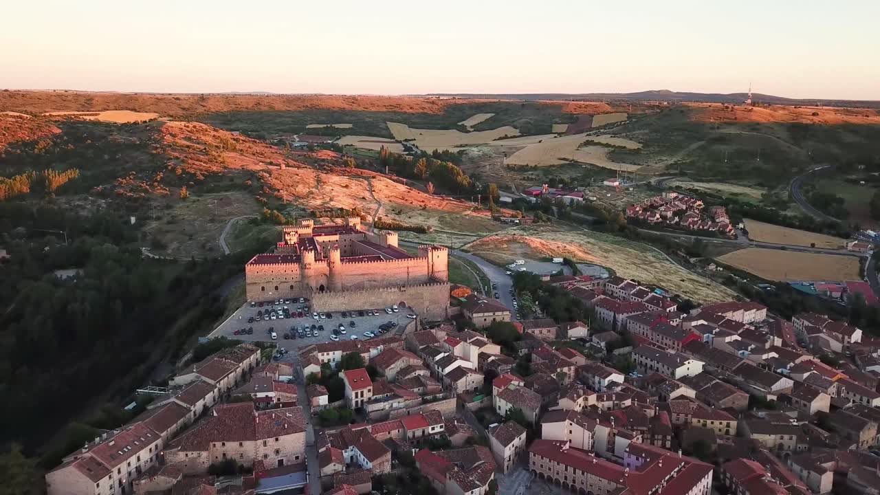 Aerial view capturing Sigüenza Castle, a stunning medieval fortress, glowing in the sunset while overlooking the historic town of Sigüenza in Guadalajara, Spain, drone pulling out