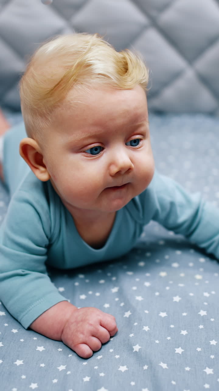 Funny baby boy with adorable plump cheeks lies in his crib. Beautiful blond infant at home. Vertical video