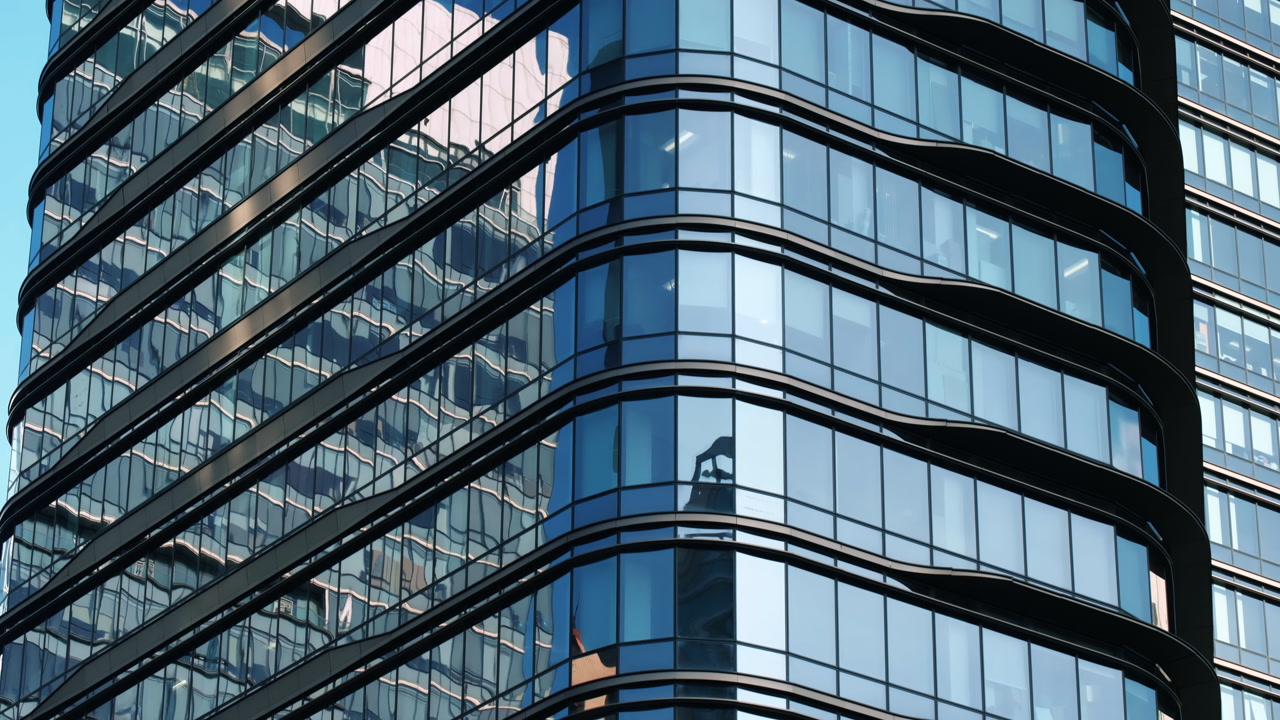 Modern walls are made of glass and steel with reflections of buildings and blue sky.